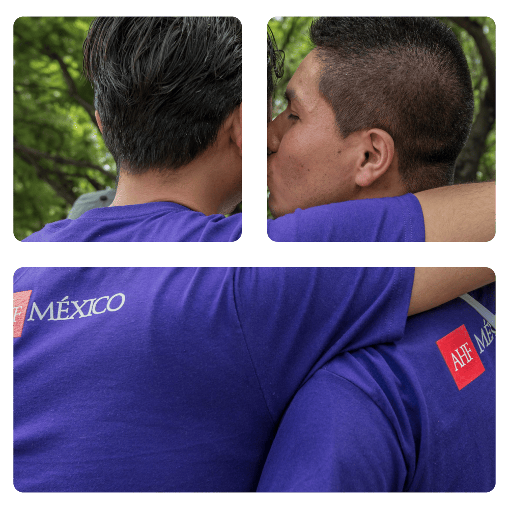 Dos hombres abrazados al aire libre, uno visto de espaldas y otro de perfil, en un entorno con árboles.