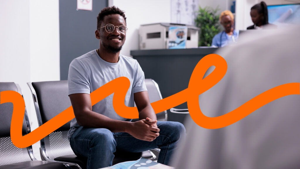 Smiling man with glasses sits in a modern waiting area with an orange graphic swoosh across the foreground.